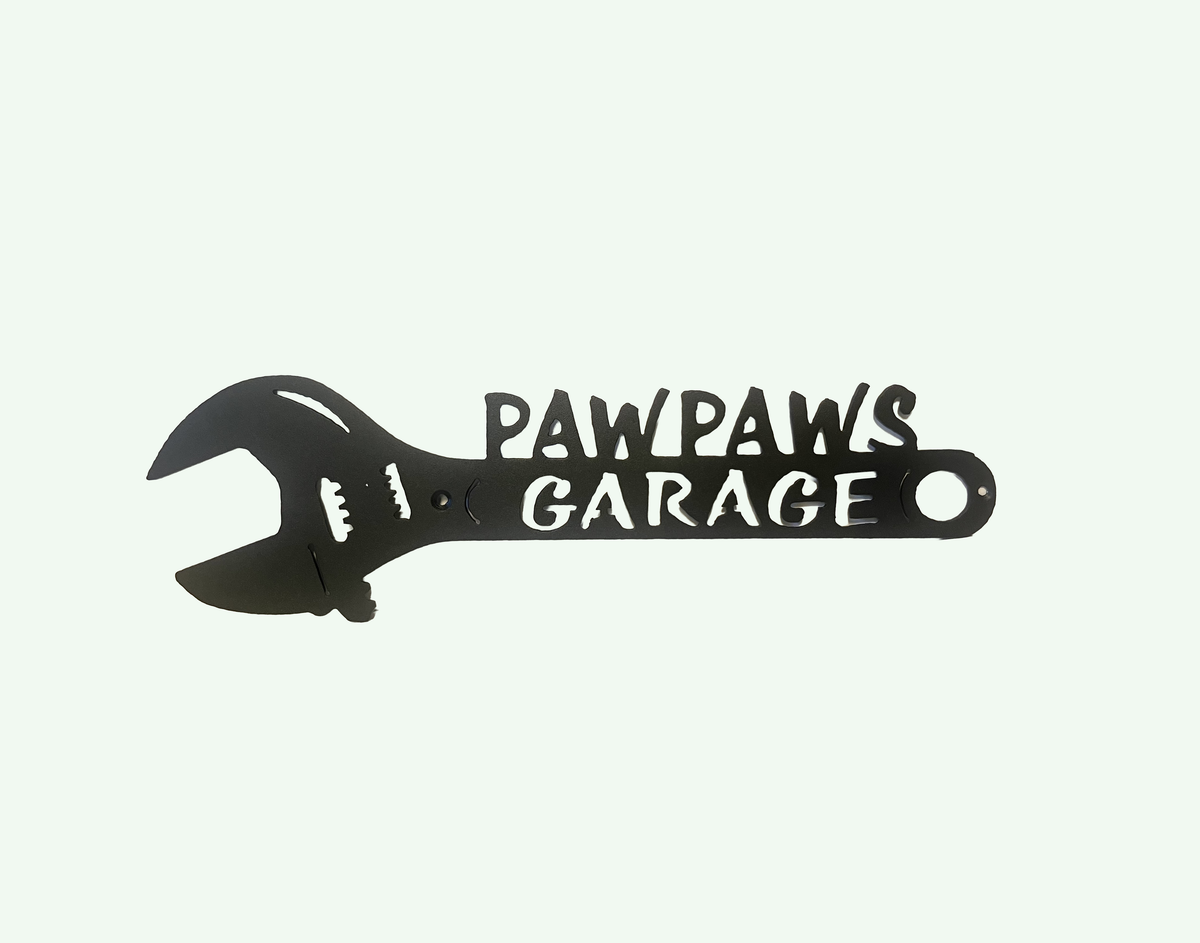 A black metal wrench-shaped wall sign with the words 'PAWPAWS GARAGE' cut into it, shown on a plain off-white background.