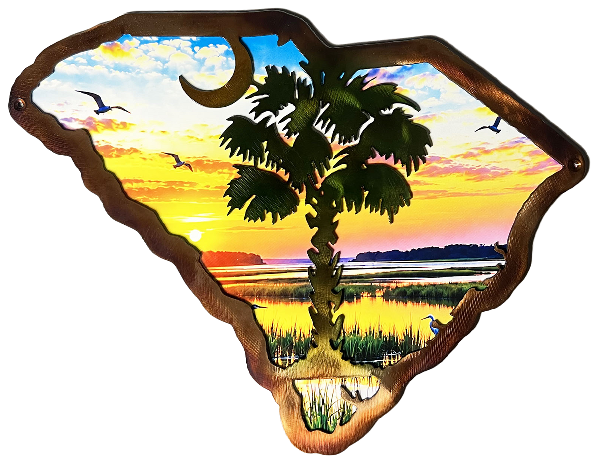 A decorative metal wall sign shaped like the state of South Carolina, featuring a colorful sunset landscape with a palm tree, marsh grass, birds, and a crescent moon, set against a plain white background.