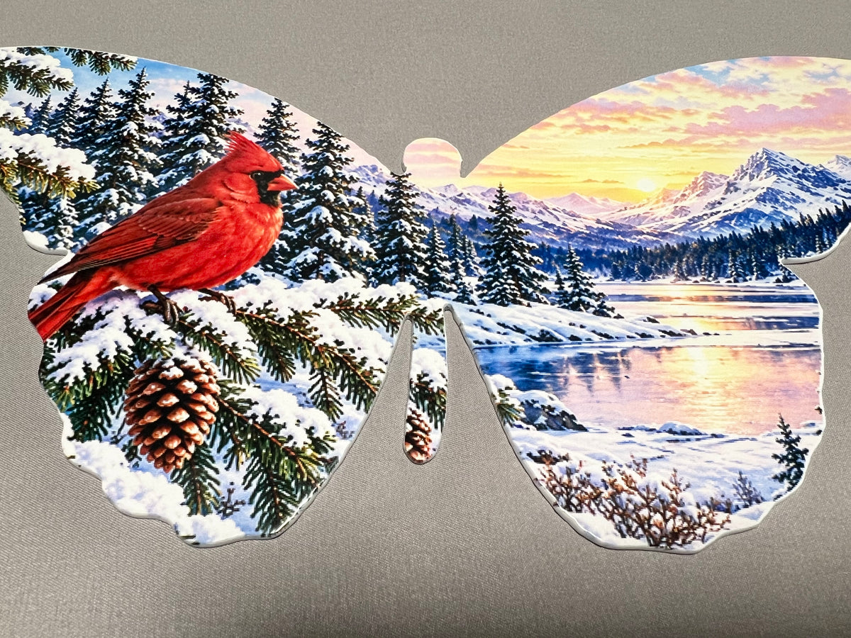 Close-up of bright red cardinal perched among snow-covered evergreen branches on butterfly-shaped metal wall art.