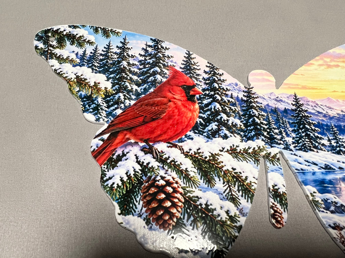 Detailed view of red cardinal, snowy pine branches, and pinecones printed on the left wing of the metal butterfly.
