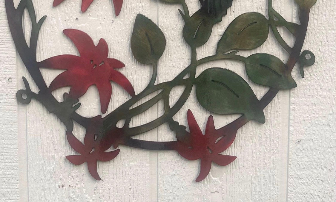 Close-up of red flowers, green leaves, and branches on hummingbird metal wall art.