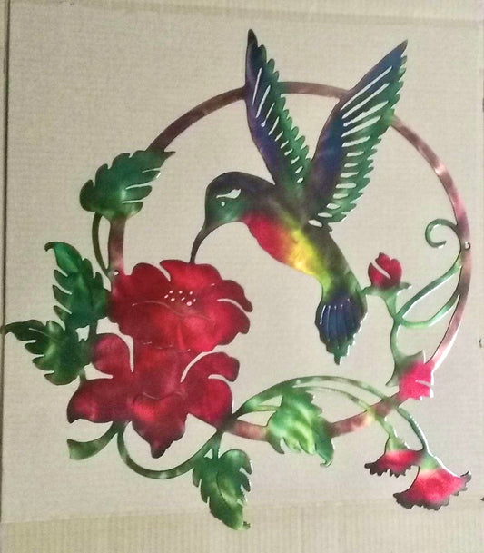 A plasma cut metal wall art depicting a colorful hummingbird feeding on a red flower, with a patina finish.
