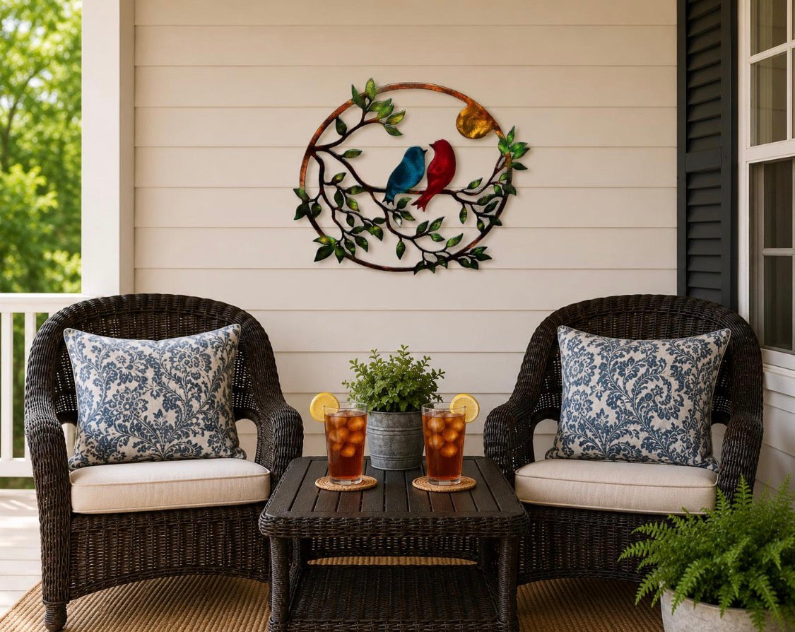 Love birds metal wall art displayed on a covered porch above wicker chairs and table.