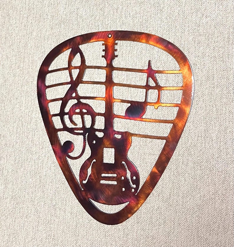 Guitar pick shaped metal wall art with guitar silhouette, treble clef, and music notes in a hand-finished multicolor patina.