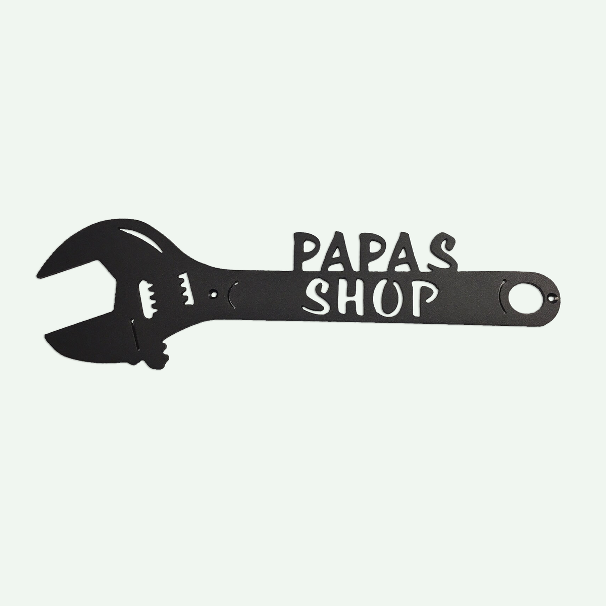 A black metal wall sign shaped like an adjustable wrench, with the words 'PAPAS SHOP' cut out in white on the handle, shown against a pale off-white background.