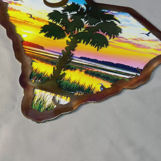 Handcrafted South Carolina palmetto metal wall art featuring a dimensional plasma-cut steel foreground over a colorful UV-printed coastal sunrise scene, with the iconic palmetto tree and crescent moon.