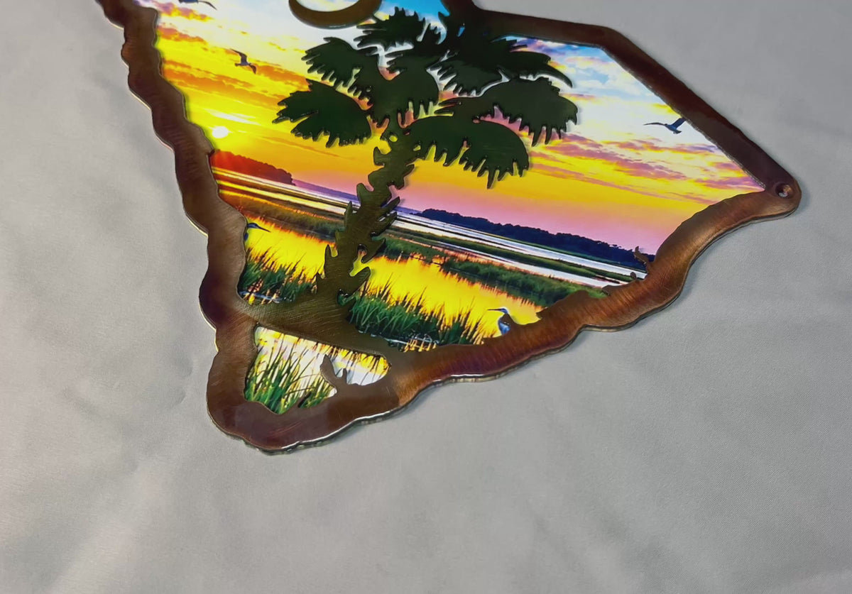 Handcrafted South Carolina palmetto metal wall art featuring a dimensional plasma-cut steel foreground over a colorful UV-printed coastal sunrise scene, with the iconic palmetto tree and crescent moon.