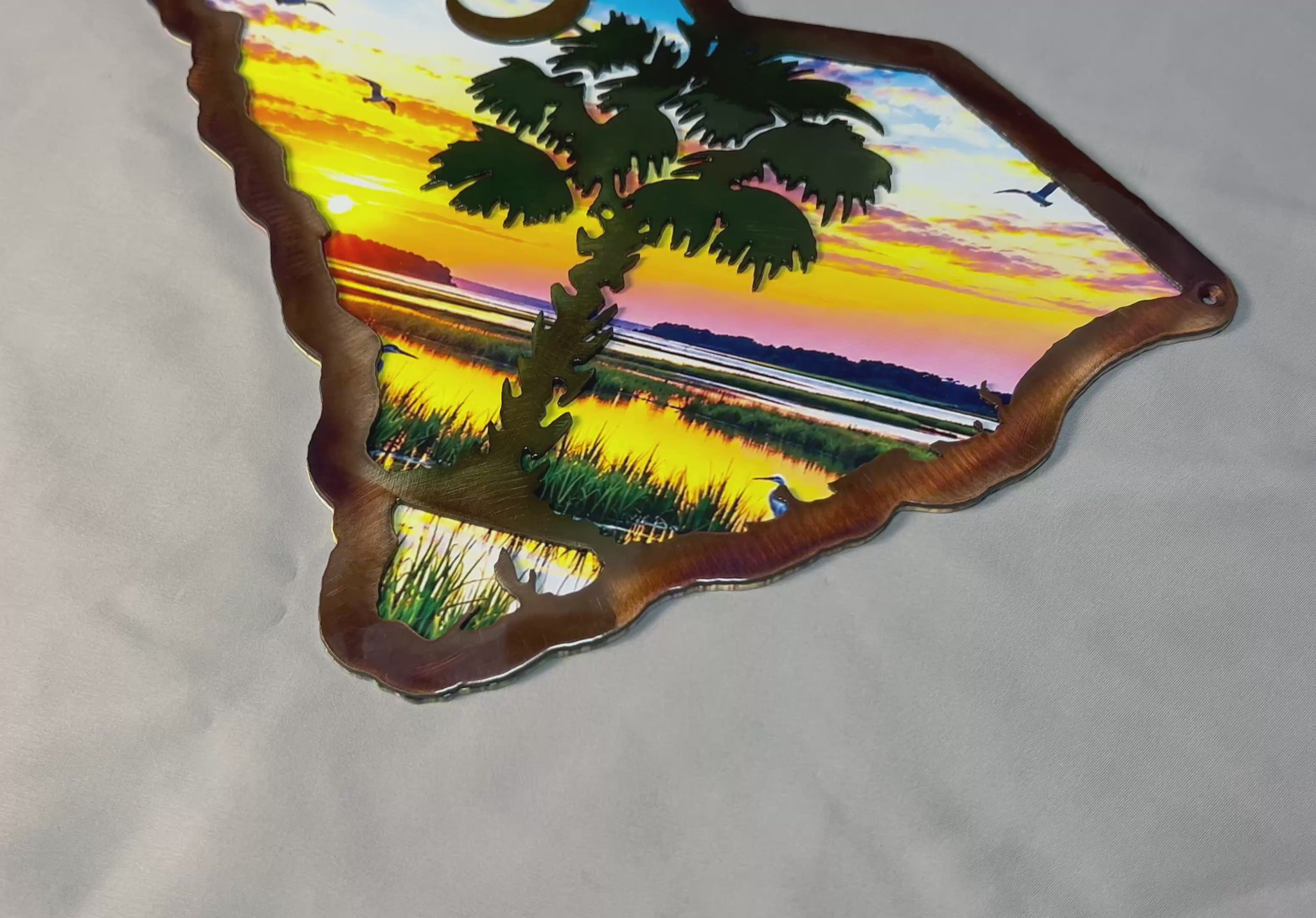 Handcrafted South Carolina palmetto metal wall art featuring a dimensional plasma-cut steel foreground over a colorful UV-printed coastal sunrise scene, with the iconic palmetto tree and crescent moon.