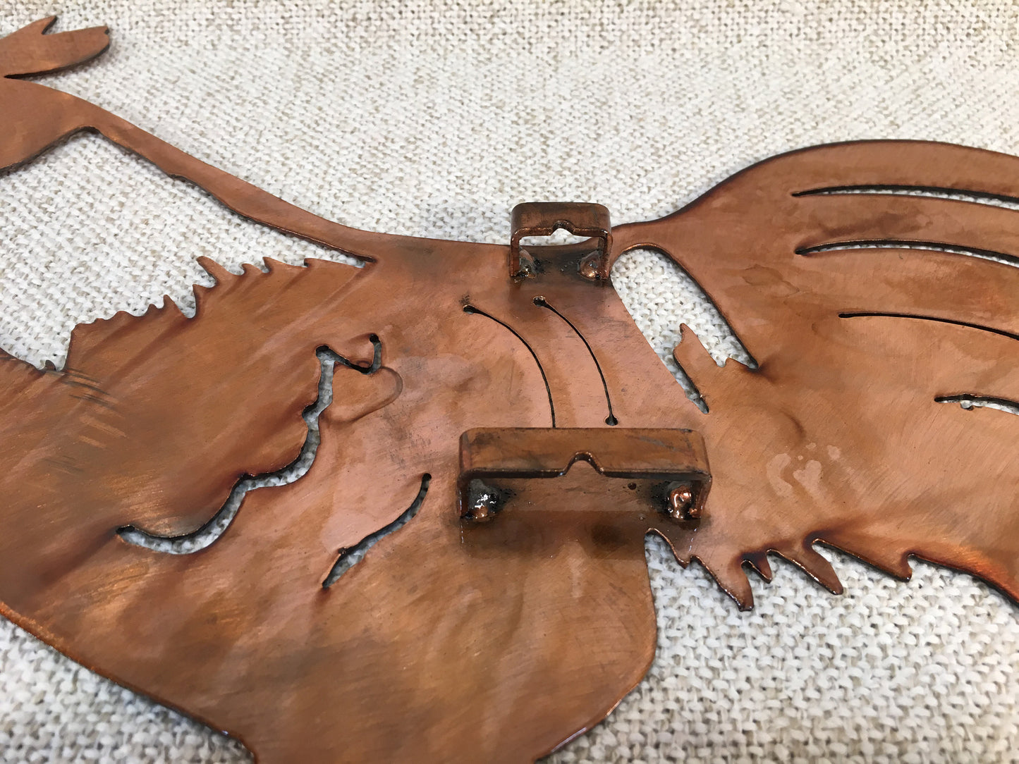 A wall-mounted metal art depiction of a rooster with a copper and patina finish, featuring airbrushed alcohol dye highlights.