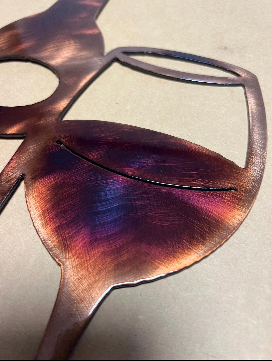 Close-up of a wine glass section showing burgundy, purple, and copper patina on the steel wall art.