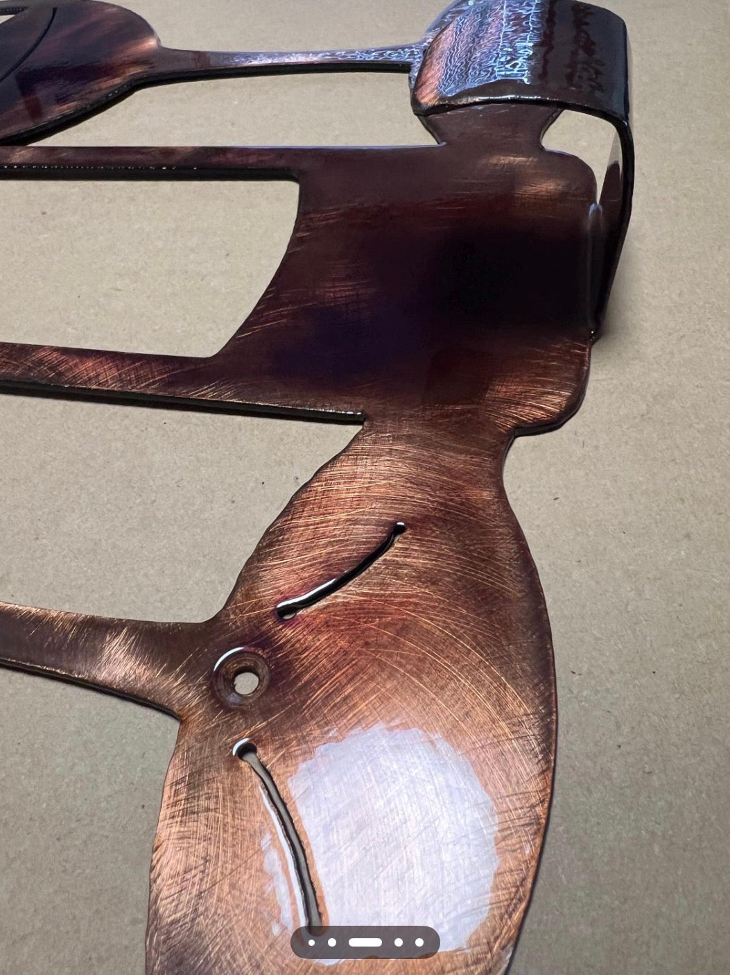 Close-up of the copper-toned hand-finished steel surface on the wine bottle towel hanger.